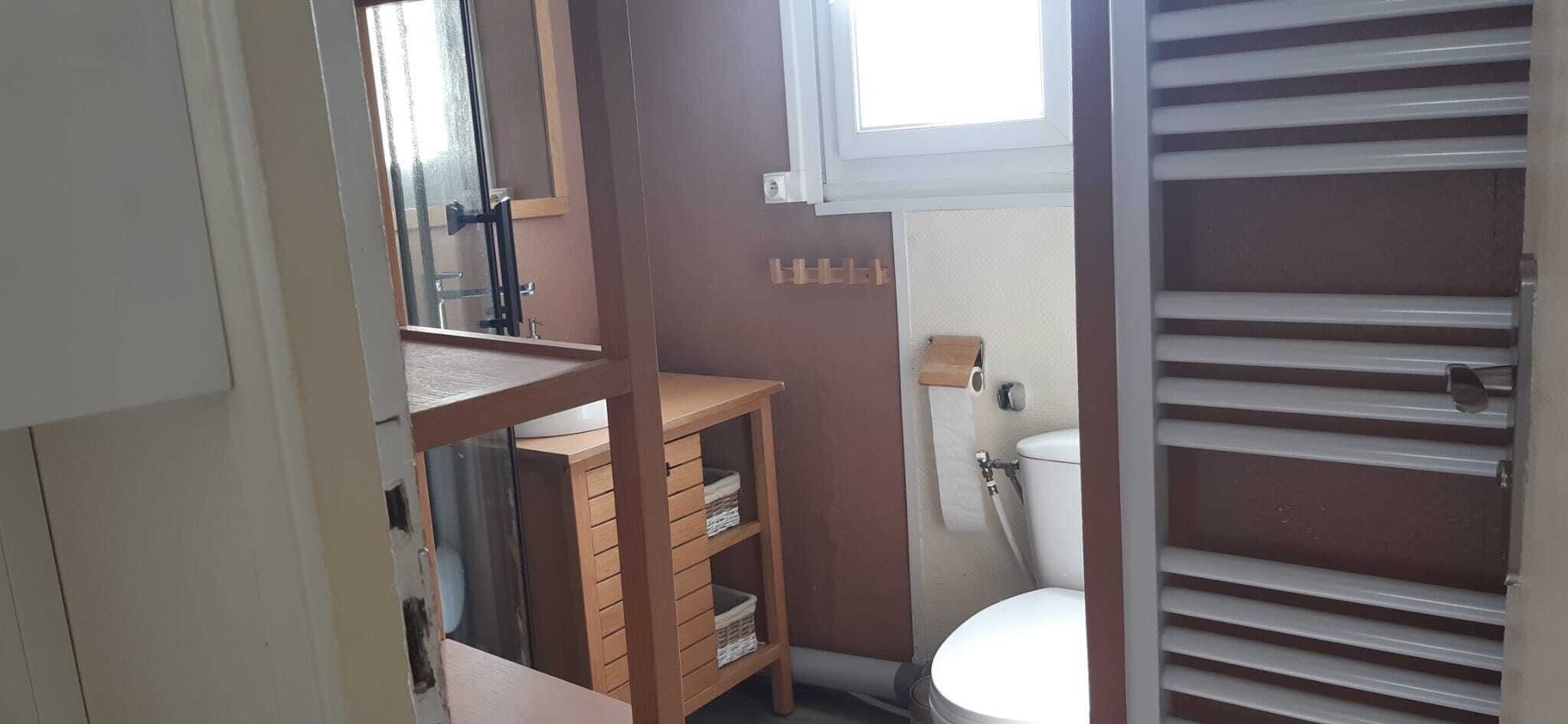 A bathroom with a toilet, a sink, a mirror, and a shelf with folded towels.