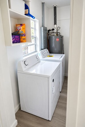 Ein Waschraum mit einer Waschmaschine und einem Trockner mit Frontlader, einem Warmwasserbereiter und Regalen für Reinigungsmittel.