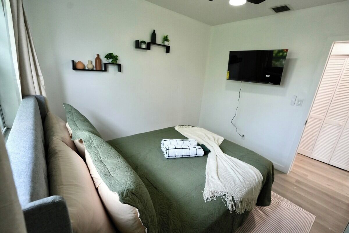 A bedroom with a bed, a TV, and a window with curtains.