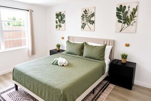 Un dormitorio con cama, dos mesitas de noche, una ventana y decoración en la pared.