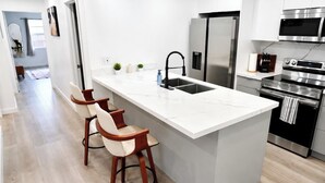 A modern kitchen with a marble island, stainless steel appliances, and wooden bar stools. - Near Hard Rock . Game Room + 15 Min to Beach (Hollywood)