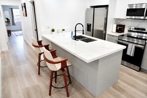 A modern kitchen with a marble island, stainless steel appliances, and wooden bar stools. - Near Hard Rock . Game Room + 15 Min to Beach (Hollywood)