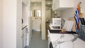 Una cocina estrecha con suelo a cuadrícula en blanco y negro, armarios blancos, un lavabo y una cafetera.