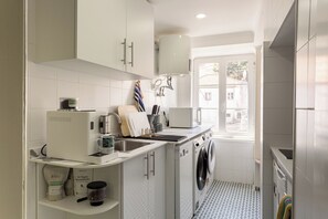 Eine kleine Küche mit Waschmaschine, Kaffeemaschine und Fenster mit Blick nach draußen.