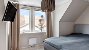 Ein modernes Schlafzimmer mit Bett, Flachbildfernseher an der Wand, einem Fenster mit Vorhängen und einer Heizung.