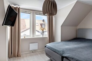Quarto moderno com cama, televisão de tela plana na parede, janela com cortinas e radiador.