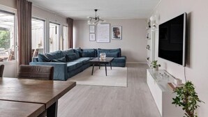 Ein modernes Wohnzimmer mit einem Ecksofa, einem Esstisch, einem flachbildfernseher an der Wand und einem großen Fenster.