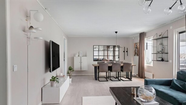 Ein modernes Wohnzimmer mit Flachbildfernseher, Essbereich mit Tisch und Stühlen sowie einem blauen Sofa.