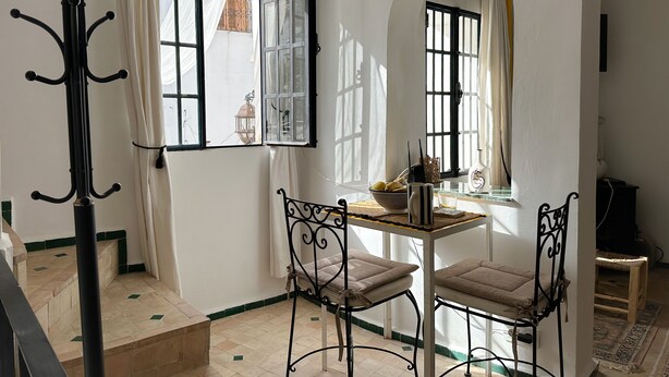 Ein Zimmer mit Esstisch, zwei Stühlen, einer Hängelampe und einem fenster mit Vorhängen.