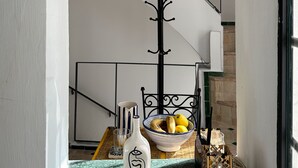 Eine Treppe mit weißer Geländer, eine Hängeleuchte und ein Tisch mit Obstschale und einer Flasche.
