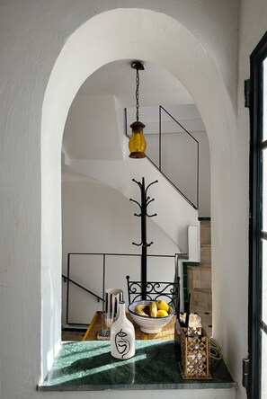 Eine Treppe mit weißer Geländer, eine Hängeleuchte und ein Tisch mit Obstschale und einer Flasche.
