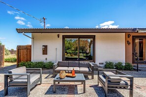 A modern outdoor seating area with a sofa, two chairs, and a table, featuring a bottle and glasses.