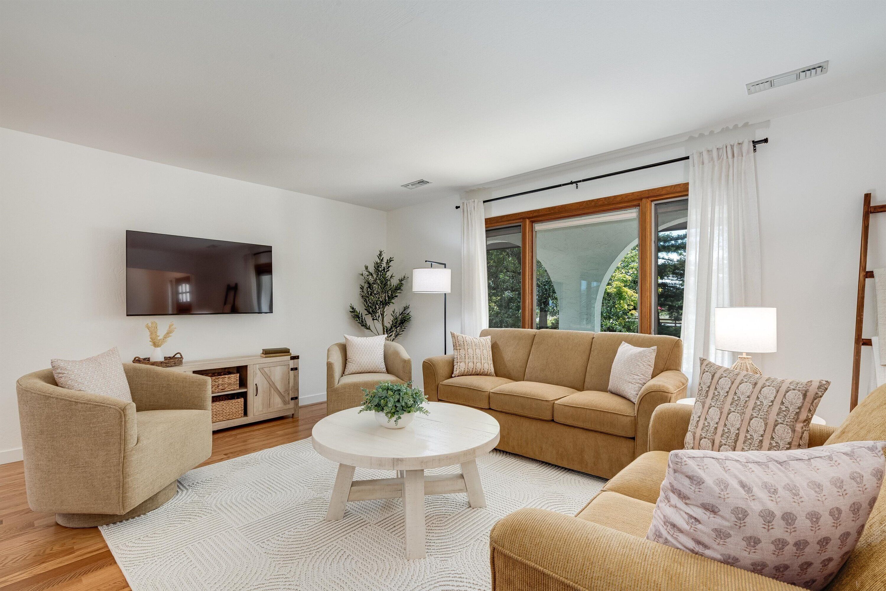 A living room with a beige sofa, a round coffee table, and a flat-screen TV mounted on the wall.