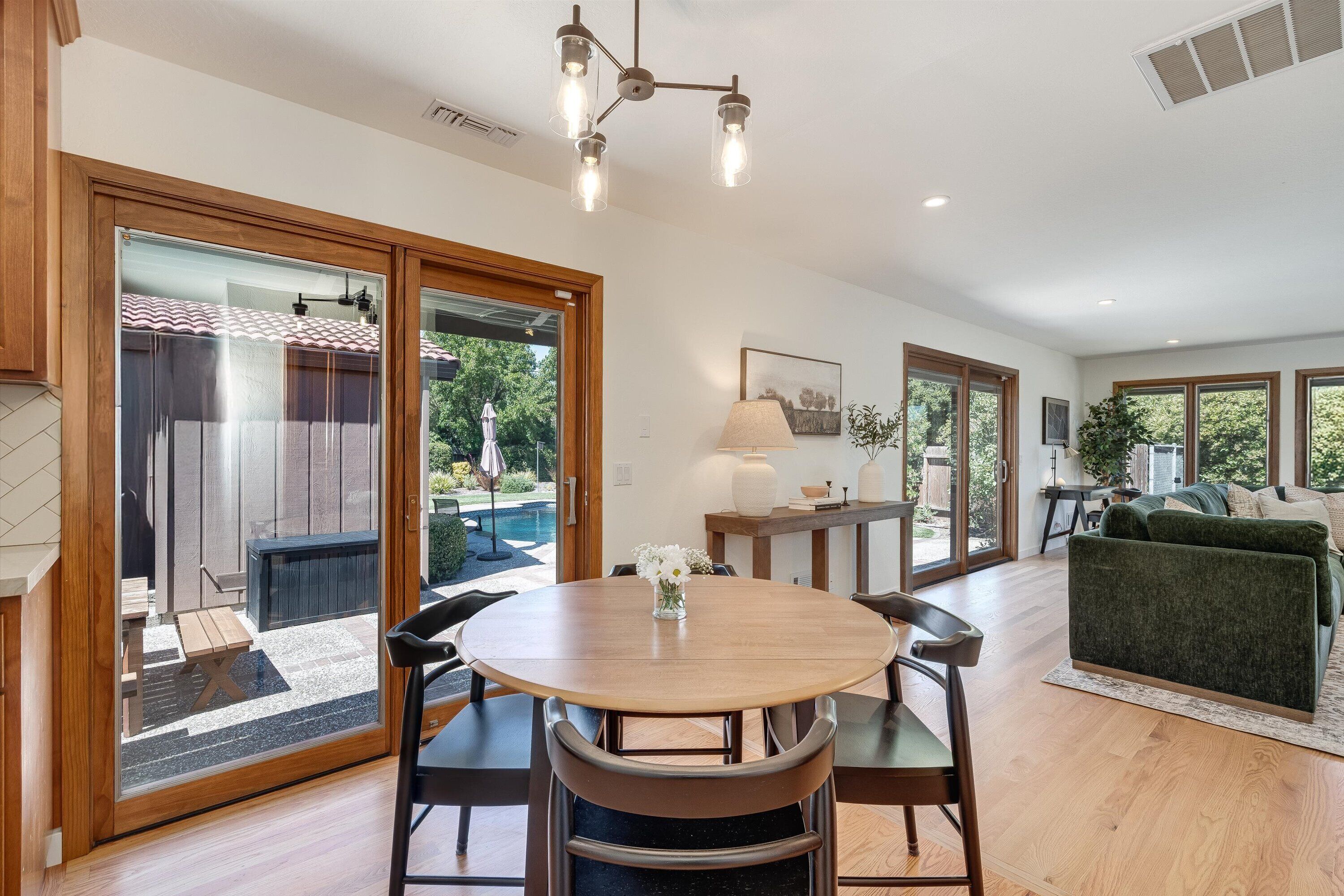 A modern interior with a dining area, a sofa, and a view of a swimming pool.