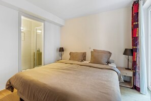 Ein Schlafzimmer mit einem Bett, zwei Nachttischlampen, einem Nachttisch und einem durchgehenden Türspalt sichtbaren Badezimmer.