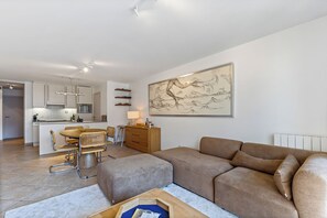 A modern living room with a brown sofa, a dining area with a round table, and a kitchen in the background. - Plaza 309/0204 + P23* (SInt Idesbald)
