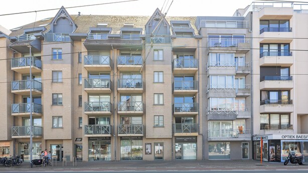 Ein mehrstöckiges Wohngebäude mit Balkonen, einem Geschäft im Erdgeschoss und einer sichtbaren Schaufensterfront.
