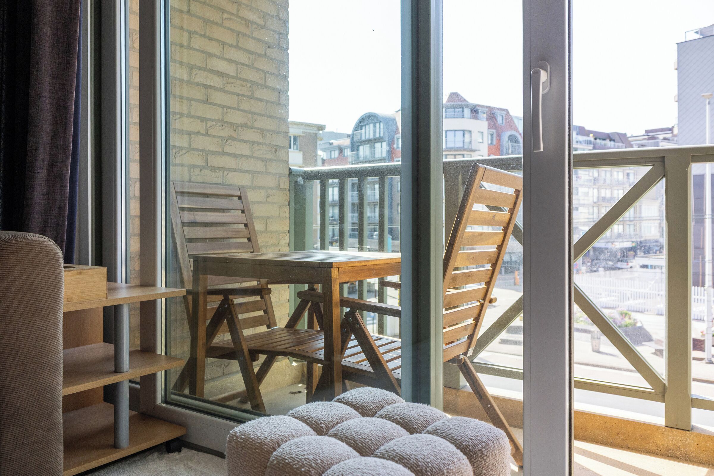 Une pièce avec une table et des chaises en bois, un canapé et une vue sur les bâtiments à travers de grandes fenêtres.