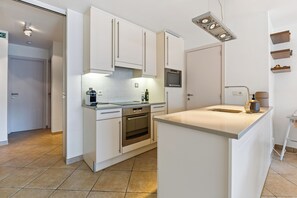 A modern kitchen with white cabinetry, a built-in oven, and a countertop island. - Plaza 309/0204 + P23* (SInt Idesbald)