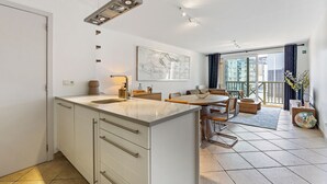 Eine moderne Küche mit einer zentralen Kochinsel, einem Essbereich mit rundem Tisch und einem Balkon mit Blick auf die Stadt.