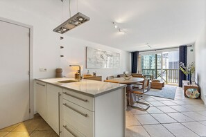 A modern kitchen with a central island, dining area with a round table, and a balcony with a view of the city. - Plaza 309/0204 + P23* (SInt Idesbald)