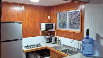 A compact kitchen with wooden cabinets, a microwave, a gas stove, a sink, and a window.