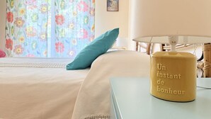 Una cama con un cojín verde azulado, una mesa con una lámpara y una pared con una cortina floral.