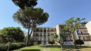 Un edificio de varios pisos con balcones, una entrada central y abundante vegetación.