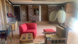 A cozy indoor seating area with a red sofa, wooden chairs, a small table, and a wicker bench. - Bungalow. Come and enjoy a family outing surrounded by nature (ozumba)