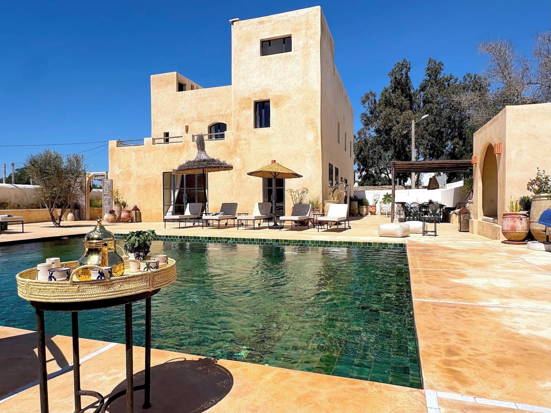 Un área de piscina con sillones de descanso y una mesa con una bandeja de objetos.
