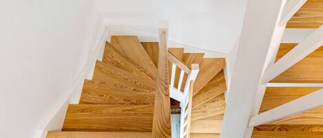 Una escalera de madera con barandillas blancas y un muro rústico.