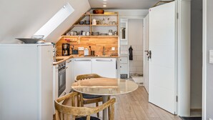Et kompakt køkken med et spisebord og stole, kaffemaskine og indbygget ovn.