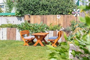A wooden deck with a table and two chairs, surrounded by a well-maintained garden with various plants and a wooden fence in the background. - Apartment 'Inselherz-Rügen' with Quiet Location and Garden Seating (Bergen auf Rügen)