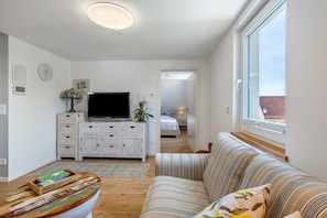 A modern living room with a sofa, a TV on a white cabinet, a wooden coffee table, and a window with a view. - Apartment 'Inselherz-Rügen' with Quiet Location and Garden Seating (Bergen auf Rügen)