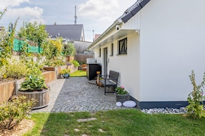 A residential backyard with a paved patio, a wooden fence, and various potted plants.
