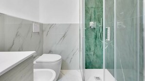 A modern bathroom with a glass shower enclosure, a toilet, and a marble-tiled wall. - CRE9 [Loreto - Cathedral] • Central • Modern • (Milano)
