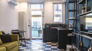 Un espace de vie compact comprenant un coin cuisine, un canapé, une table à manger et un téléviseur posé sur une étagère.