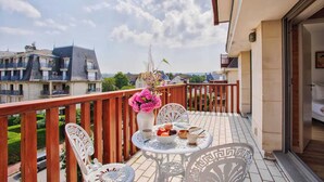 Un balcón con una mesa lista para el desayuno, un jarrón de flores y vistas a edificios cercanos.