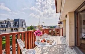 A balcony with a table set for breakfast, a vase of flowers, and a view of neighboring buildings. - Charming Apt w/ Large Balcony - 2bd/4p -deauville (Deauville)