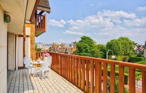 A balcony with a table and chairs, a wooden railing, and a view of the neighborhood. - Charming Apt w/ Large Balcony - 2bd/4p -deauville (Deauville)