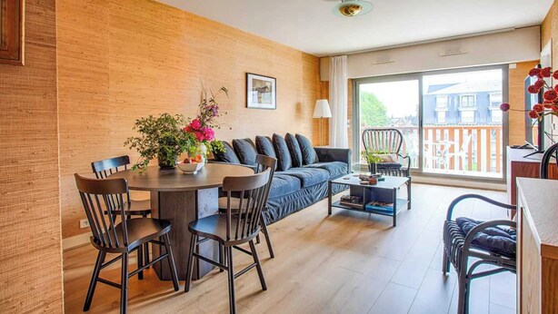 Una sala de estar moderna con sofá, mesa de comedor, sillas y un balcón con vistas.