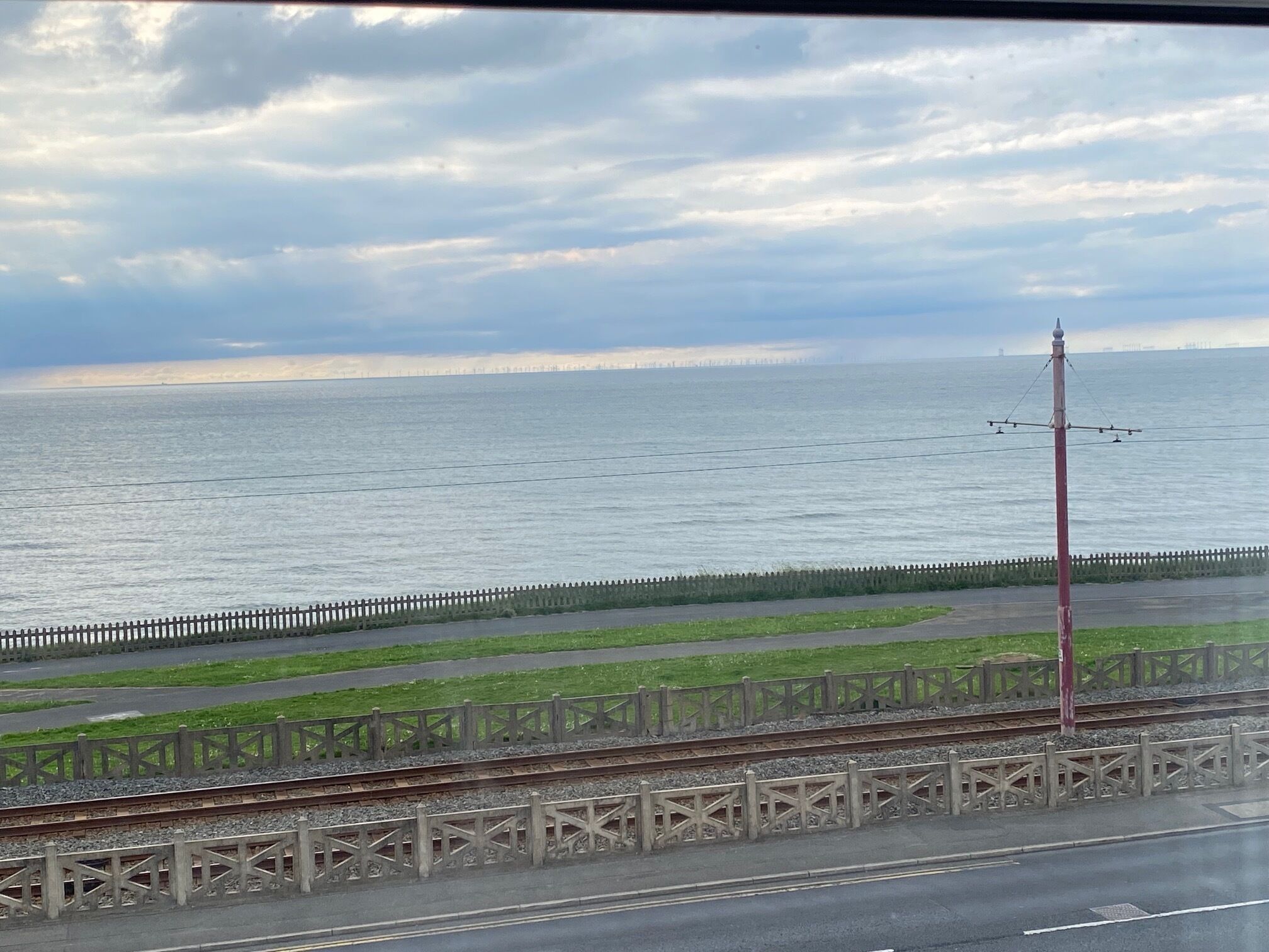 A coastal view with a railway track, a fence, and a cloudy sky.