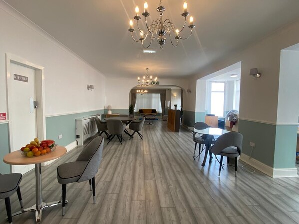 A spacious dining area with a chandelier, a kitchen sign, and a fruit bowl on a table.