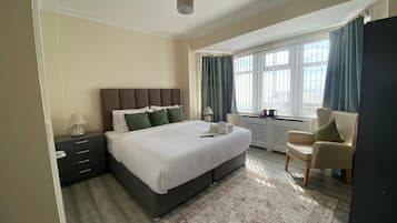 Un dormitorio moderno con una cama grande, una mesita de noche, una silla y una ventana con cortinas.
