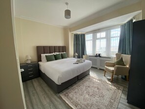 A modern bedroom with a large bed, a bedside table, a chair, and a window with curtains.
