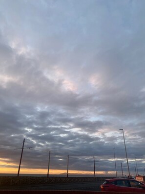 Una carretera costera con un coche rojo, farolas y un cielo nublado.