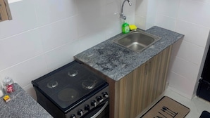 A kitchen with wooden cabinets, a granite countertop, a stove, and a sink. - G.BlissHomes | Stylish Modern Studio Near Nairobi CBD with King Bed & Work space (Nairobi)