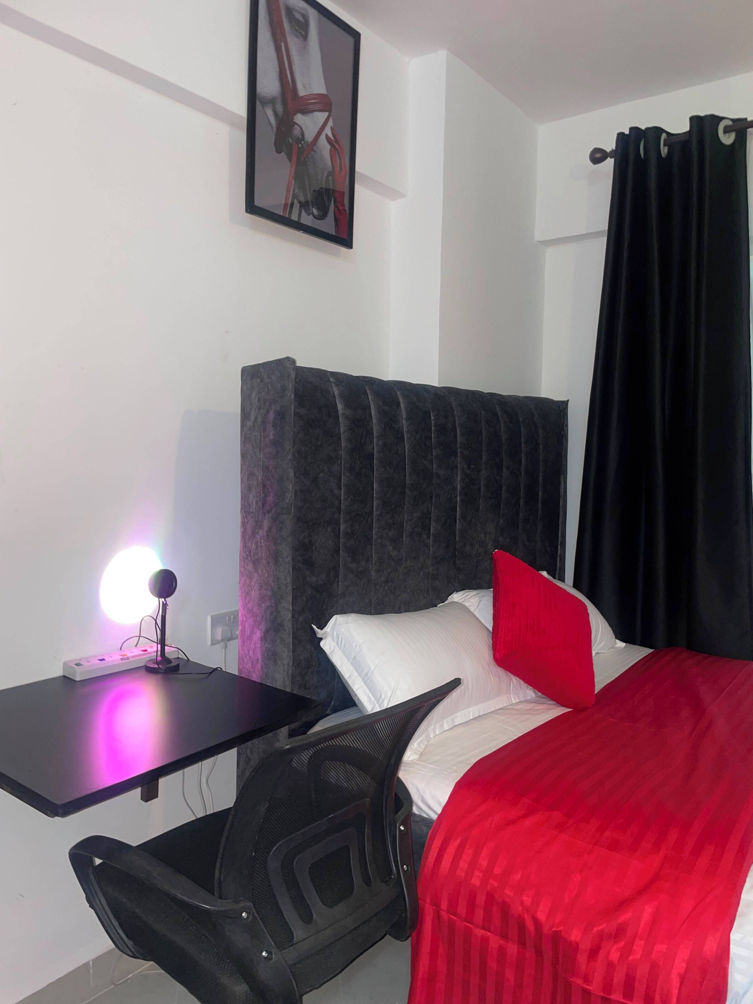 Une chambre d’hôtel comprenant un lit, un bureau, une chaise, une table de chevet et un tableau accroché au mur.