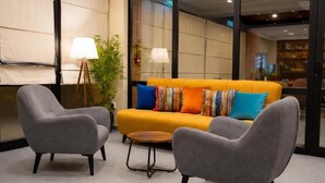 Un hall moderno con un sofá amarillo, sillones grises, una pequeña mesa redonda y una lámpara.