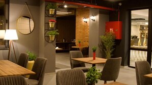 Un comedor moderno con mesas y sillas de madera, plantas en macetas y una pared de ladrillo.